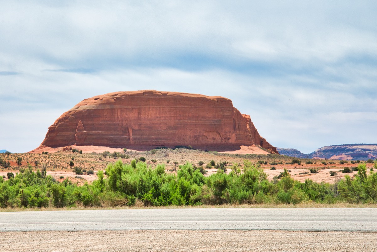 A broad red sandstone butte rising from desert scrub beside a highway